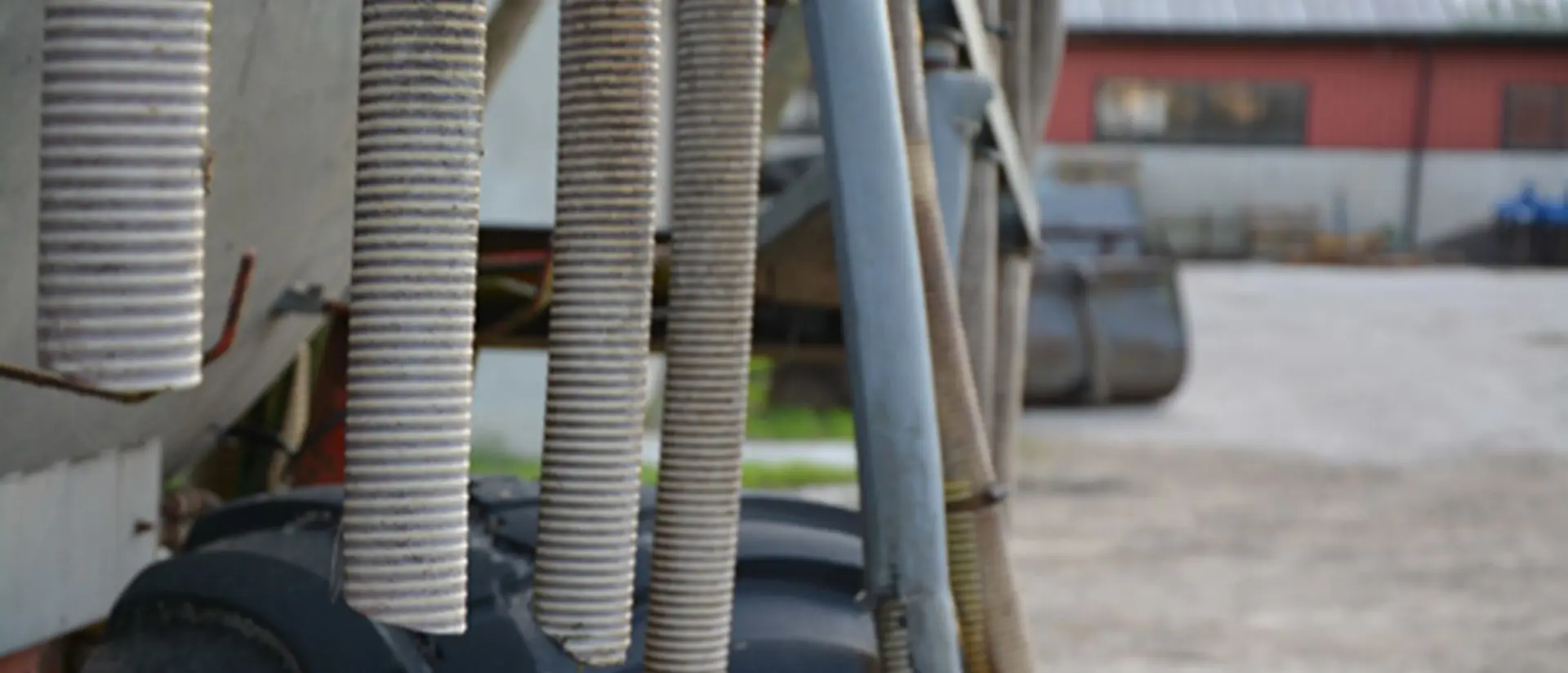 Slangar som hänger ner från en jordbruksmaskin. Maskinen står på gårdsplan på ett lantbruk.